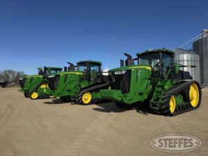 Tre gröna bandtraktorer av märket John Deere står uppradade utomhus.