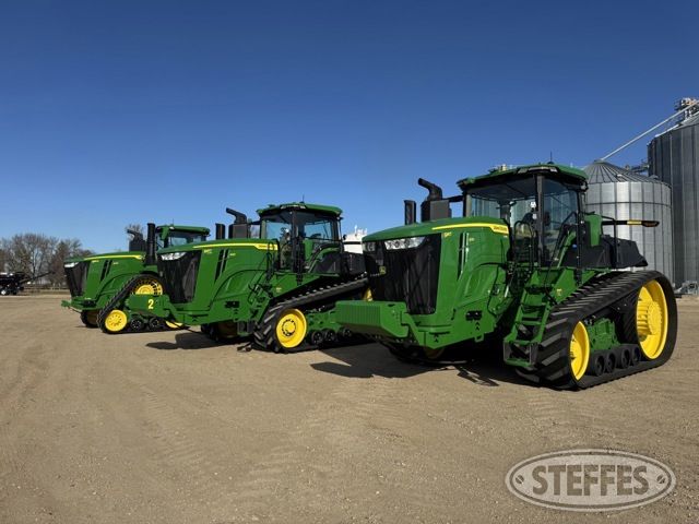 Tre gröna bandtraktorer av märket John Deere står uppradade utomhus.